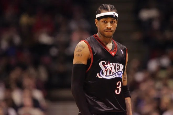 Allen Iverson wearing a black Sixers jersey with the number 3, showing a focused expression during a game.