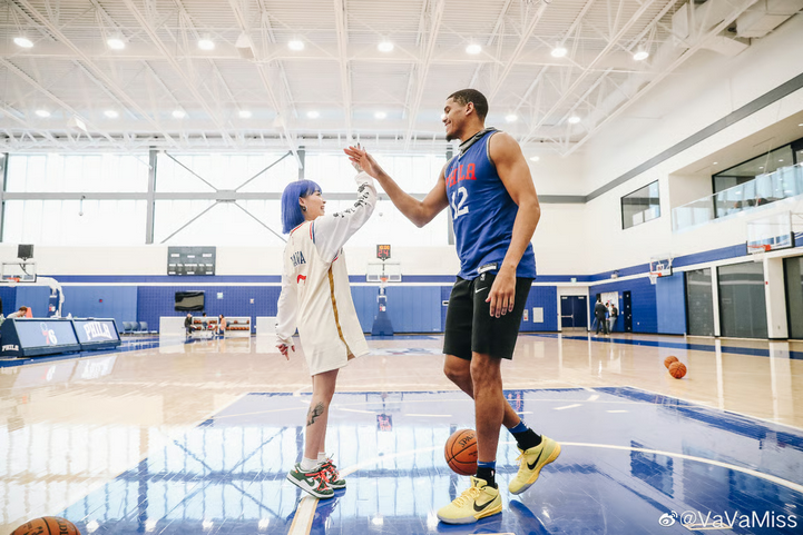 Chinese rapper VaVa interacts with NBA player Tobias Harris during a training session, both smiling and posing with basketballs in a gym setting.